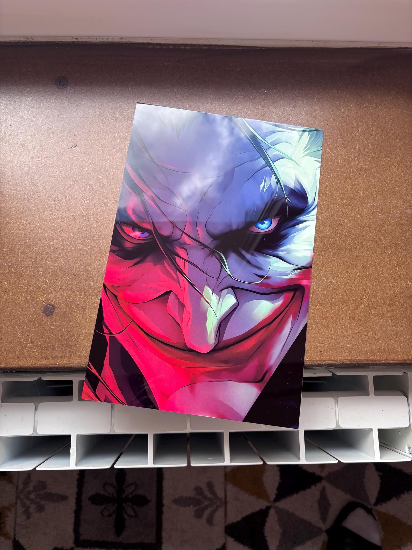 Tableau métallique en aluminium brillant représentant un gros plan du visage du Joker avec un sourire menaçant, éclairé par une lumière néon rouge à gauche et bleue à droite.