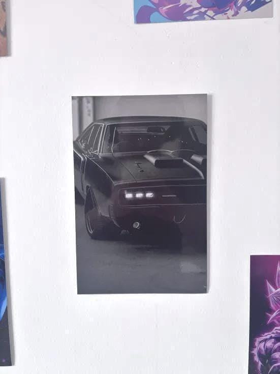 Peut inclure: Une affiche murale en noir et blanc représentant une voiture de sport classique vue de face. Le véhicule présente une prise d'air proéminente sur le capot, des phares rectangulaires éclairés et une silhouette basse. L'image capture la voiture dans un cadre sombre et contrasté, soulignant les lignes épurées de la carrosserie et le design détaillé de la calandre avant.