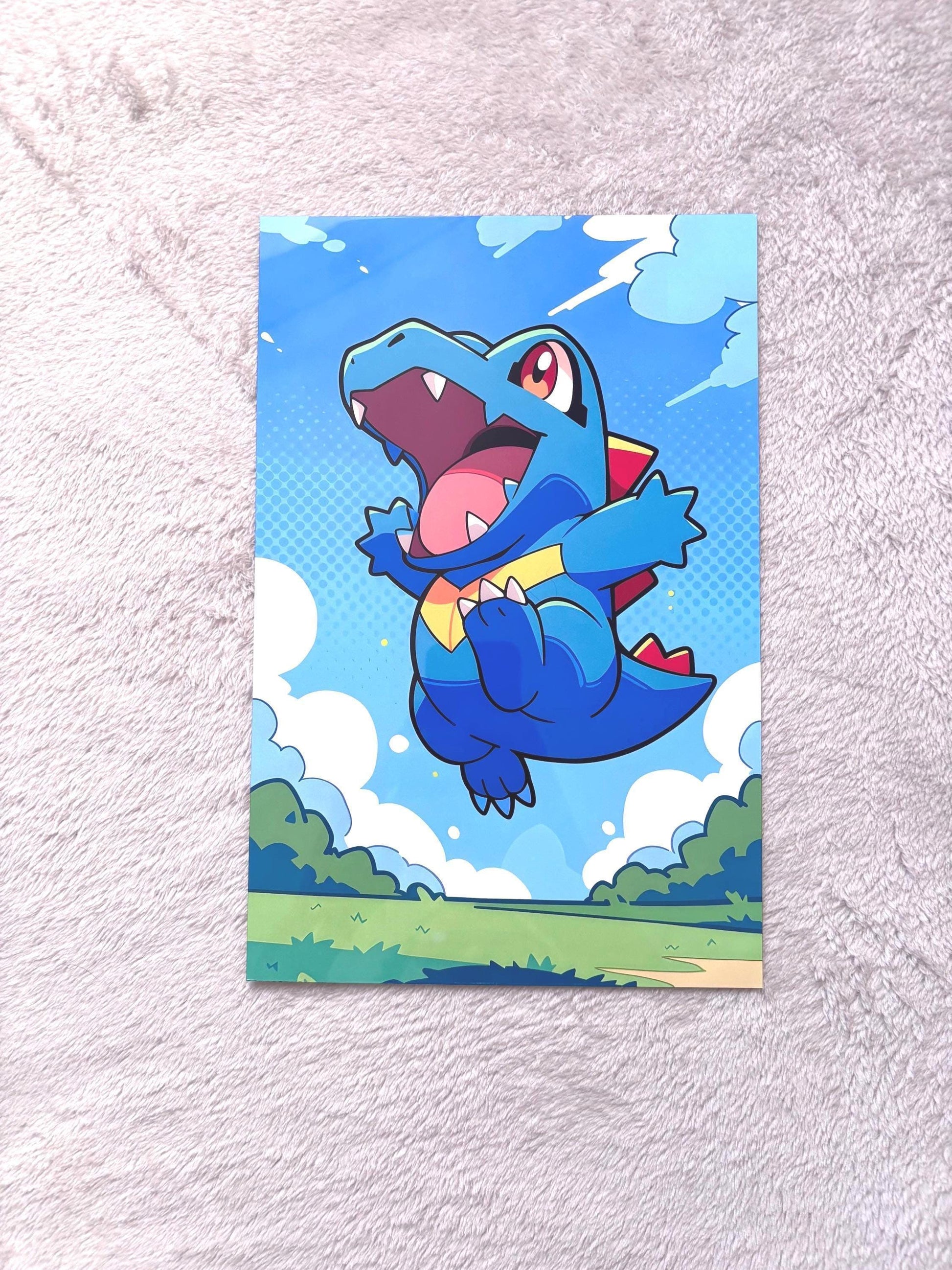 A colorful cartoon-style illustration of a blue alligator-like creature with a large open mouth, flying through a blue sky with clouds and green grass below.
