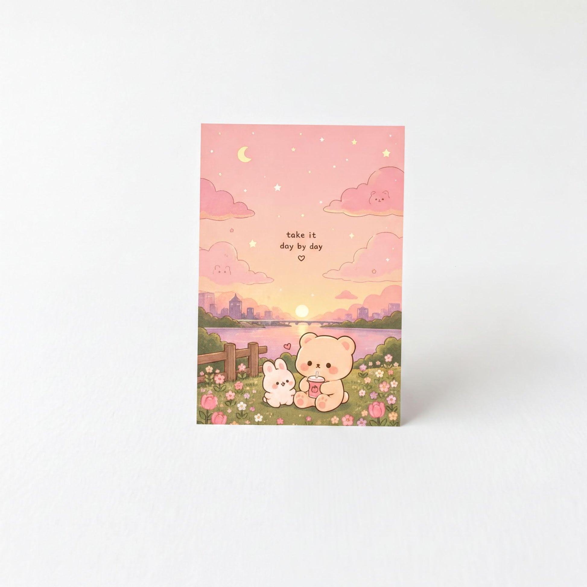 A greeting card with a pink and purple background depicting a serene scene with a bunny, a bear, and a rabbit sitting together in a field with flowers, under a crescent moon and stars.