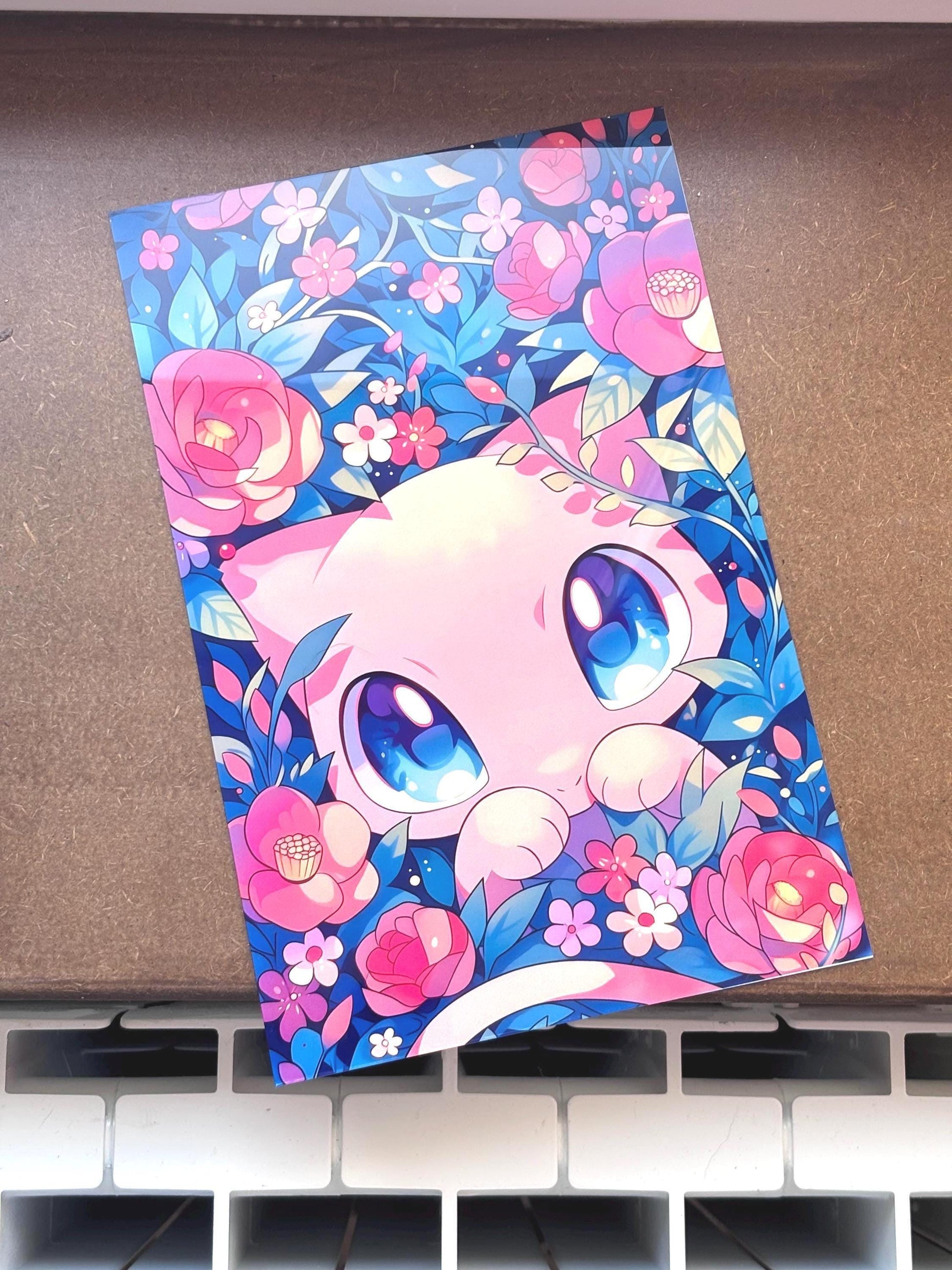 Tableau métallique en aluminium brillant représentant le Pokémon légendaire Mew regardant vers le haut avec de grands yeux bleus, entouré de roses roses et de feuilles bleues et violettes.