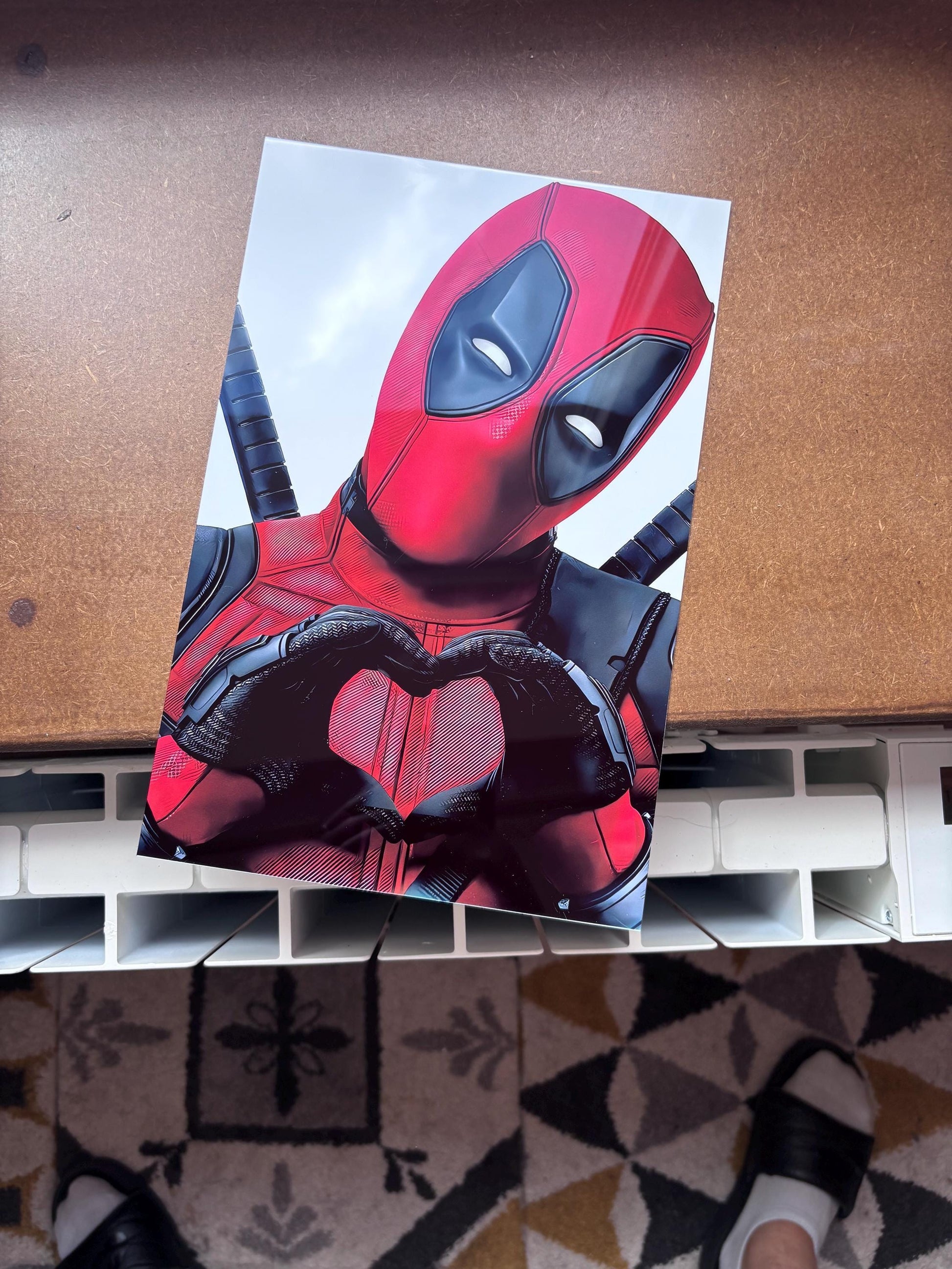 Tableau métallique en aluminium brillant représentant Deadpool de face, bras croisés avec des katanas dont les poignées portent le logo Deadpool, dans un style néon lumineux rouge vif sur un fond dégradé sombre bleu-violet, avec le texte néon DEADPOOL en bas.